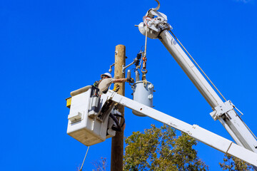 Utility worker is repairing equipment on power lines from lift truck under clear blue sky.