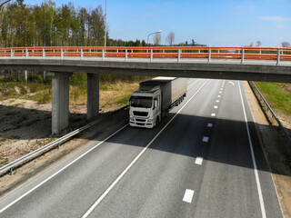 Truck drives under an overpass on a clear day along a quiet highway in a rural area