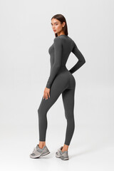Fitness woman in jumpsuit. Athletic girl on the gray background