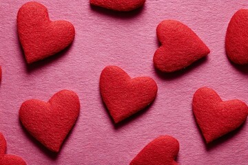 Fototapeta premium Colorful red felt hearts scattered on a vibrant pink surface create a visually appealing backdrop for celebrations and romantic occasions