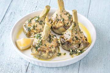 Four Roman-style artichokes served on white plate, tender and beautifully seasoned