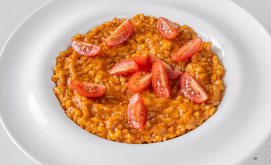 Creamy tomato risotto topped with cherry tomatoes on clean white plate