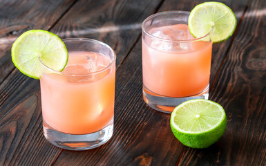 Two guava margaritas with lime wheels glow against rich dark cocktail backdrop