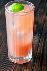 Guava Collins cocktail sparkles in tall glass with lime against dark backdrop
