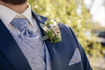 Bräutigam im eleganten blauen Anzug mit floraler Ansteckblume im Freien