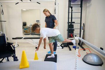 Specialist monitors a young patient performing a balance various