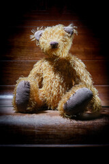 Teddy bear without eyes on a closed wooden piano.