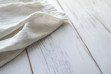 Obraz premium A close-up of a soft, white linen fabric draped over a rustic wooden surface. The texture of the fabric contrasts with the weathered wood, creating a serene and minimalist aesthetic.
