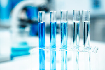 Test tubes filled with blue liquid arranged in a metal rack next to a microscope, representing scientific research, chemical analysis, and biotechnology in a modern laboratory setting.