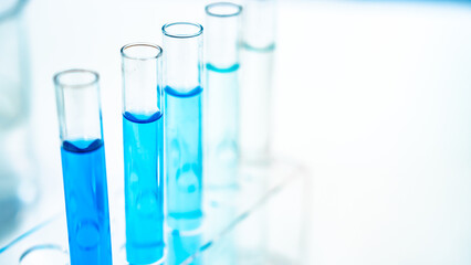 Test tubes filled with blue liquid arranged in a metal rack next to a microscope, representing scientific research, chemical analysis, and biotechnology in a modern laboratory setting.