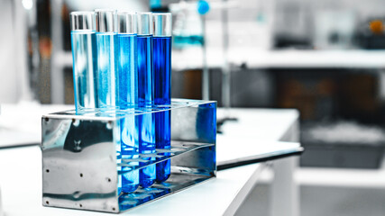 Test tubes filled with blue liquid arranged in a metal rack next to a microscope, representing scientific research, chemical analysis, and biotechnology in a modern laboratory setting.