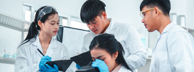 Group of young scientists or students working together in a laboratory, using a microscope and...