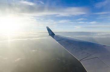 Obraz premium Airplane wing in foreground with soft evening light casting hues of orange and blue. Vast cloudscape and horizon stretch beneath, offering tranquil aerial view. Captured from passengers perspective
