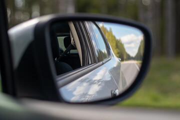 Side mirror view from a moving car showing a clear highway bordered by trees under a sunny sky with...