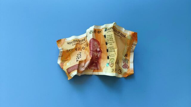 Single crumpled two hundred indian rupee currency bank note isolated on blue background. Stop motion extreme closeup top view. India inflation, money devaluation and bad economy creative concept.
