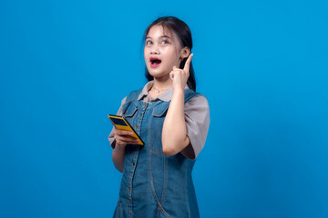 An astonished young woman, holding a smartphone, looks up with a eureka gesture, signifying a...