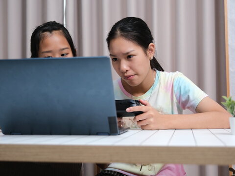 Two girls are sitting at a table looking at a laptop