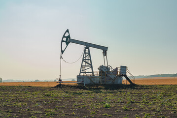 A large oil pump jack operates in an open field, extracting crude oil