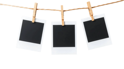 Three blank black polaroids hanging on wooden clothespins on a string isolated on transparent background