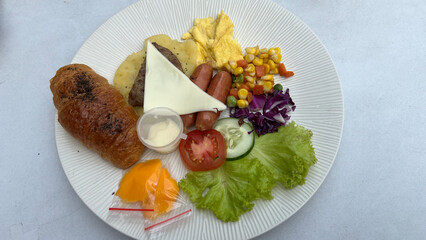 Healthy breakfast of scrambled eggs, sausage, cheese, salad, vegetable, and tomato