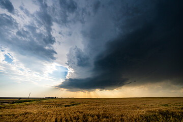Powerful supercell storm spins across open plains under a dramatic sky, filled with moving clouds,...