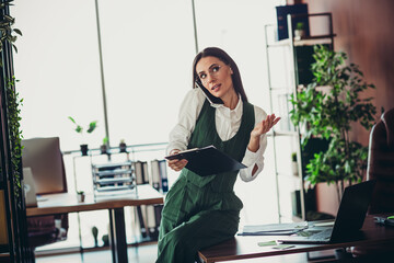 Confident businesswoman discussing work in a stylish modern office, multitasking while managing...