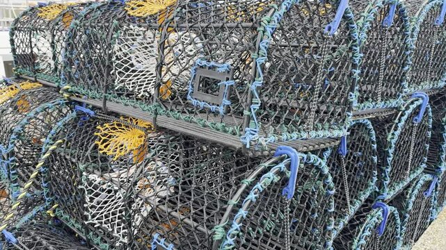 Closeup slow pan shot of mesh lobster and crab pots (also called D creels) stacked in layers, in a UK harbour quay.