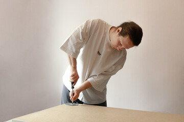 Wide-frame image of man fixing circular hardware onto a flat surface using a screwdriver. Captured...