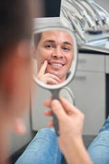 Excited client of dental clinic looking in mirror on his natural-looking veneers