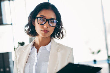 Charming businesswoman wearing glasses and formalwear, posing in an office setting for a...