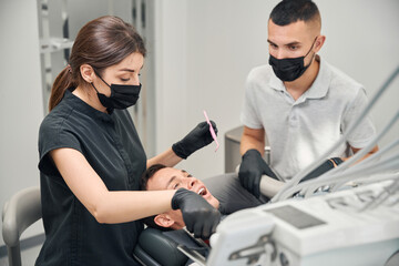 Team of skilled stomatologist in protective face masks treating patient teeth