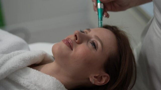 Close-up of female patient receiving rejuvenation treatment in cosmetology clinic. Professional beautician performing mesotherapy treatment to young woman focusing on skin rejuvenation, hydration.