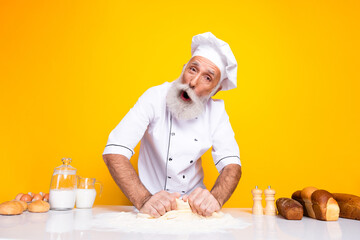 Experienced male baker enthusiastically kneading dough in a chef's uniform surrounded by baking...