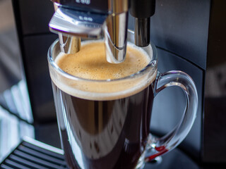 Coffee machine and glass mug with fragrant coffee. Coffee in the morning in a glass mug. Breakfast or lunch drink. Choosing a quality coffee machine