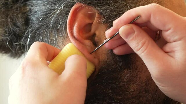 Close-up of a man carefully piercing another person's ear with a sterile needle. A staged procedure using clean instruments. Demonstration of a do-it-yourself ear piercing in a safe home environment