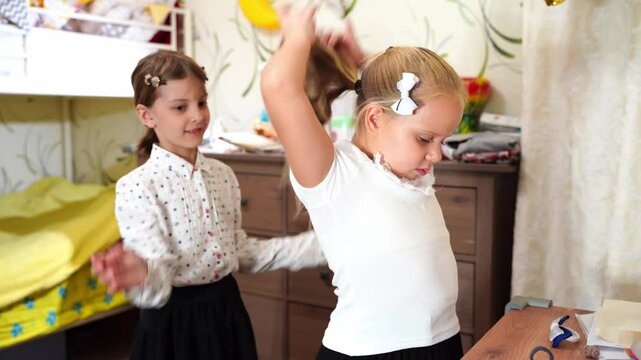 Two little girls friends getting ready for school in bedroom. Kid braids sisters hair. Children wear school uniforms. Morning routine. Doing homework, home lessons. Education back to school concept