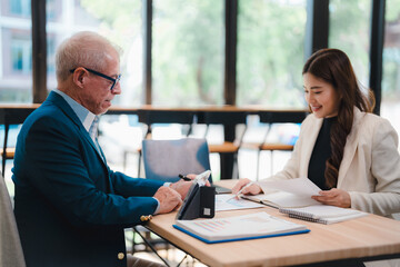Senior businessman and young businesswoman collaborating in a modern office, analyzing financial...