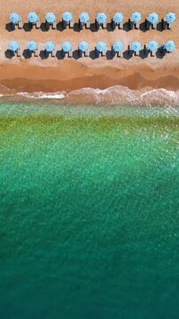 Top-down view of sandy beach with sun umbrellas and turquoise sea water