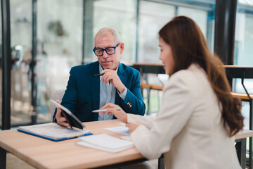 Senior businessman holding a digital tablet while discussing business plans with a businesswoman during a collaborative meeting in a modern office environment