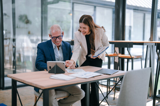 Senior businessman and young businesswoman discussing over digital tablet while working on new project in modern office, business teamwork concept