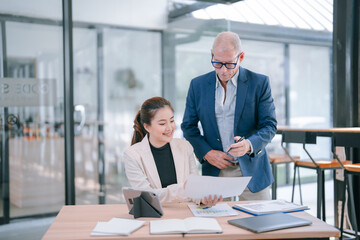 Senior manager coaching young asian businesswoman reviewing paperwork, analyzing financial charts...