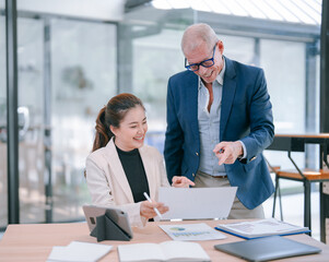 Senior manager and young businesswoman are smiling and analyzing financial reports together in modern office, discussing company performance and growth