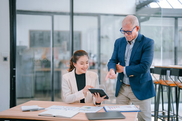 Senior manager coaching young businesswoman using tablet and analyzing financial charts while...