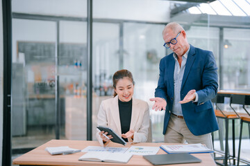 Senior manager coaching young businesswoman while analyzing financial charts and paperwork at a...