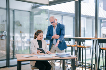 Senior manager explaining marketing strategy to young businesswoman using tablet and documents, working together in modern office, teamwork and cooperation concept