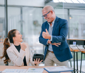 Senior businessman and young businesswoman celebrating good news in the office, giving thumbs up to signify their partnership and teamwork, embodying business success and motivation