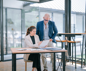 Senior manager and young businesswoman collaborating in a modern office, reviewing documents and discussing business strategy to achieve project success