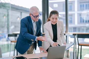Senior manager coaching and training a young businesswoman while analyzing financial charts and...
