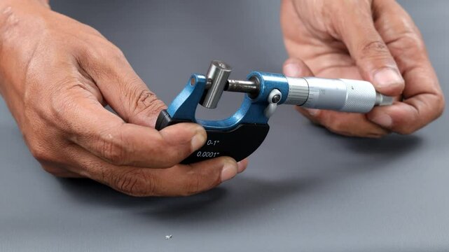 Hand holding analogue micrometer or diff micrometer quality control check roundness tube over grey table. use screw gauge calipers analogue. quality control concept.
