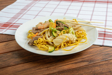 Delicious Stir-Fried Noodles Adorned With Fresh Vegetables and Savory Meat Served on a Rustic Wooden Table